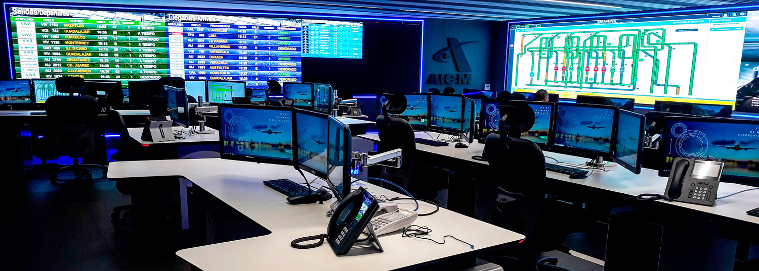 Vista panorámica del Centro de Control Operativo del Aeropuerto. Decenas de monitores en las estaciones de trabajo y en la pared del fondo muestran un flujo constante de información, incluyendo horarios de aerolíneas, destinos y diagramas técnicos, mientras varios operadores supervisan las actividades.