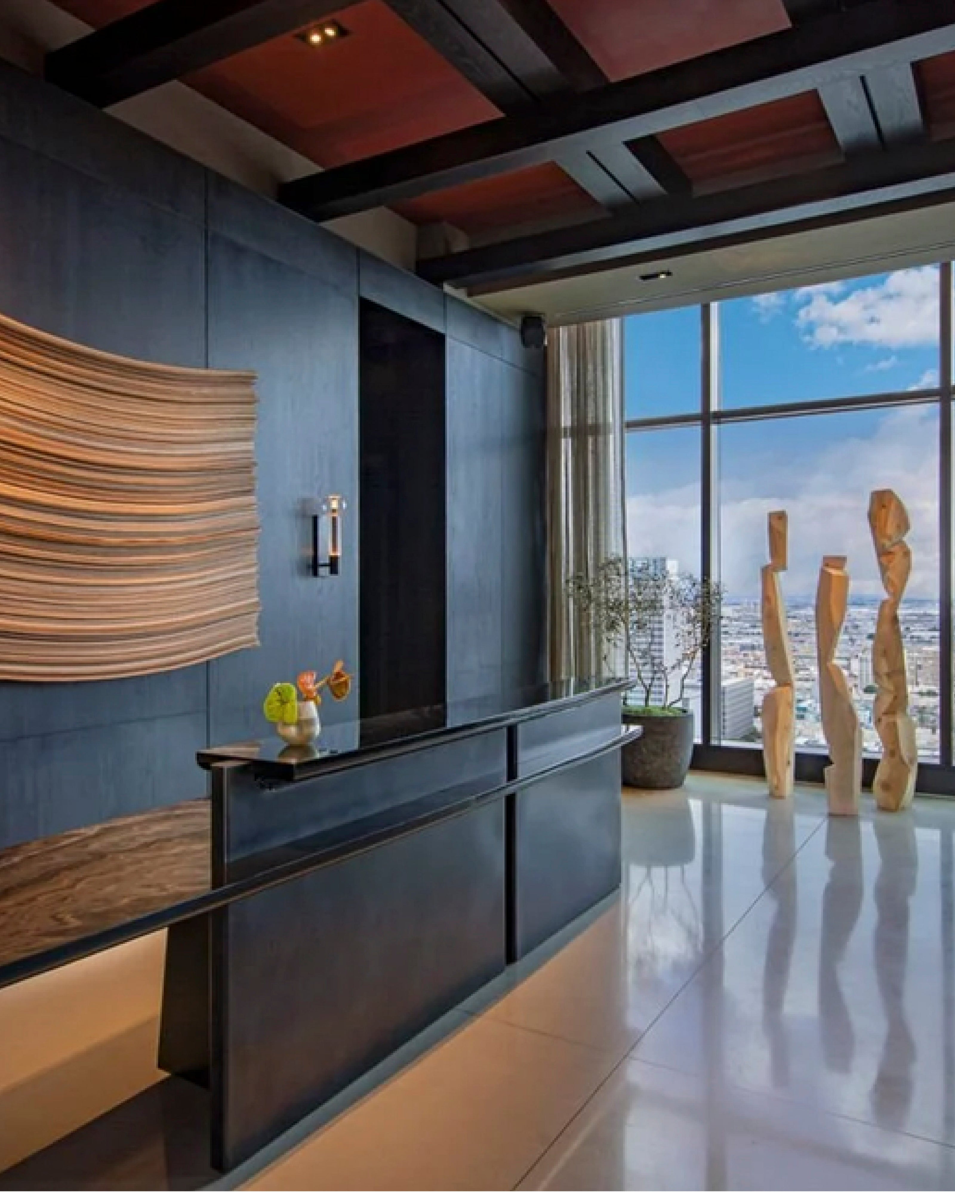 Recepción de hotel de lujo con diseño minimalista, que muestra un mostrador oscuro, paredes texturizadas y grandes ventanales con vista a la ciudad, integrando altavoces discretos en las esquinas superiores para el sistema de audio ambiental.